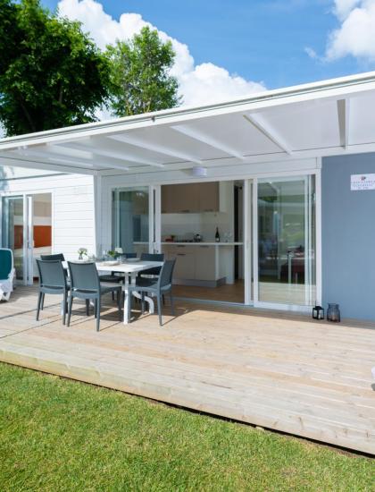 Veranda luminosa, sedie eleganti, prato verde, cielo azzurro, atmosfera rilassante.