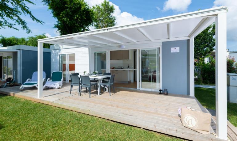 Veranda luminosa, sedie eleganti, prato verde, cielo azzurro, atmosfera rilassante.