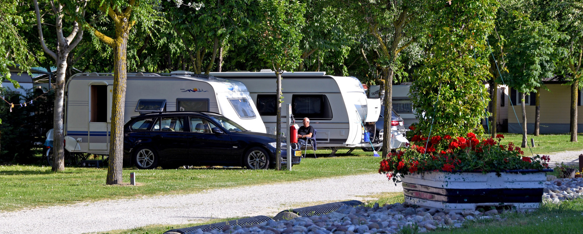 Campingplatz mit Wohnwagen, schwarzem Auto und roten Blumen.