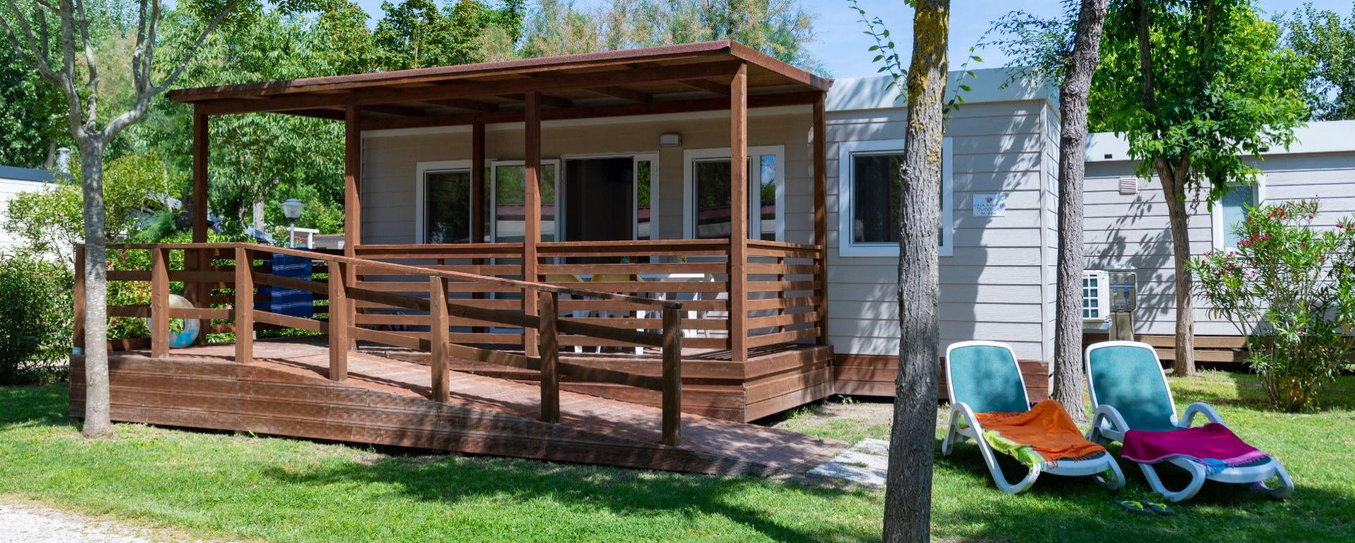 Casetta in legno con veranda e sdraio su prato verde.