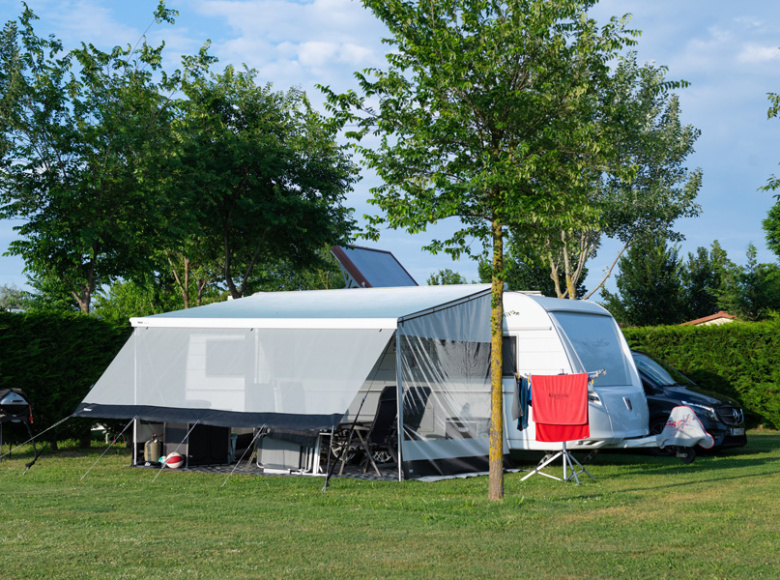 Wohnwagen mit Vorzelt auf Campingplatz, umgeben von Bäumen und grünem Rasen.